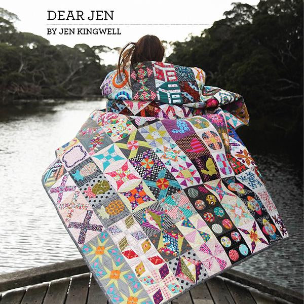 The image shows a woman standing on a dock at a river with a bright, vibrant quilt wrapped around her, flowing in the wind. Text at the top left says “Dear Jen by Jen Kingwell.”