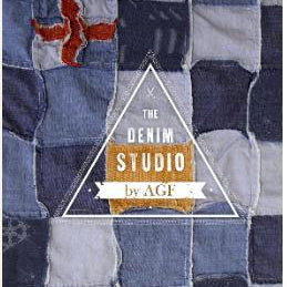 The image shows a quilt of blue denim fabric squares with a red accent in the top left corner. The text “The Denim Studio by AGF” is overlayed inside of a white triangle.