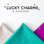 At the top of the image and centered is the text "Lucky Charms by Figo Studio." Along the bottom are five fabric cuts folded into triangles, point up like mountains. The fabrics are black, gray, aqua, magenta, and burnt orange.