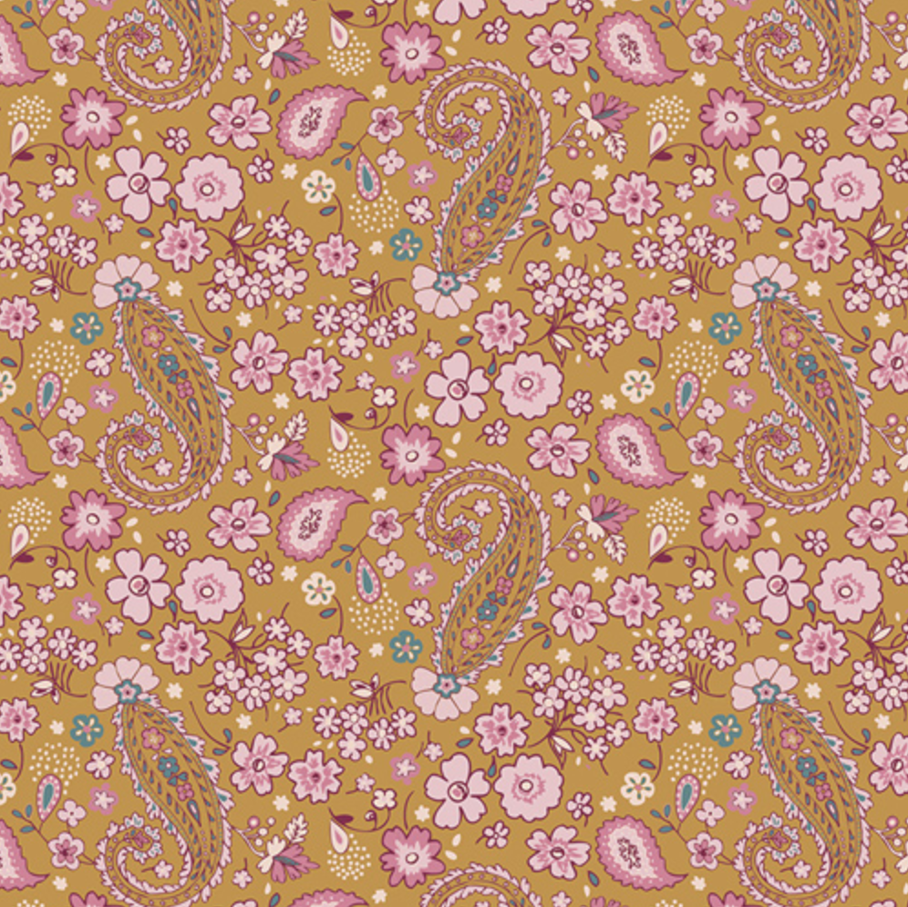 A close-up of a floral and paisley patterned fabric or wallpaper sample on a mustard yellow background, with pink flowers, pink and blue paisley motifs, and a white inch ruler along the bottom edge for scale.