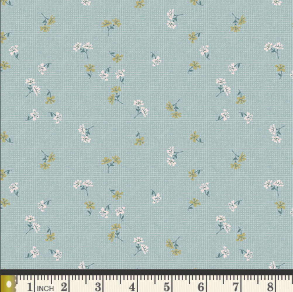A fabric pattern swatch showing a light blue-green background with a small-scale floral print in white, yellow, and green, with a measuring ruler along the bottom edge.