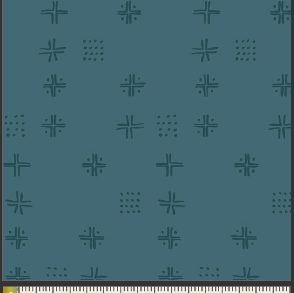 A close-up of a teal fabric pattern featuring repeating dark teal geometric motifs, with a cream-colored fabric ruler visible along the bottom edge for scale.