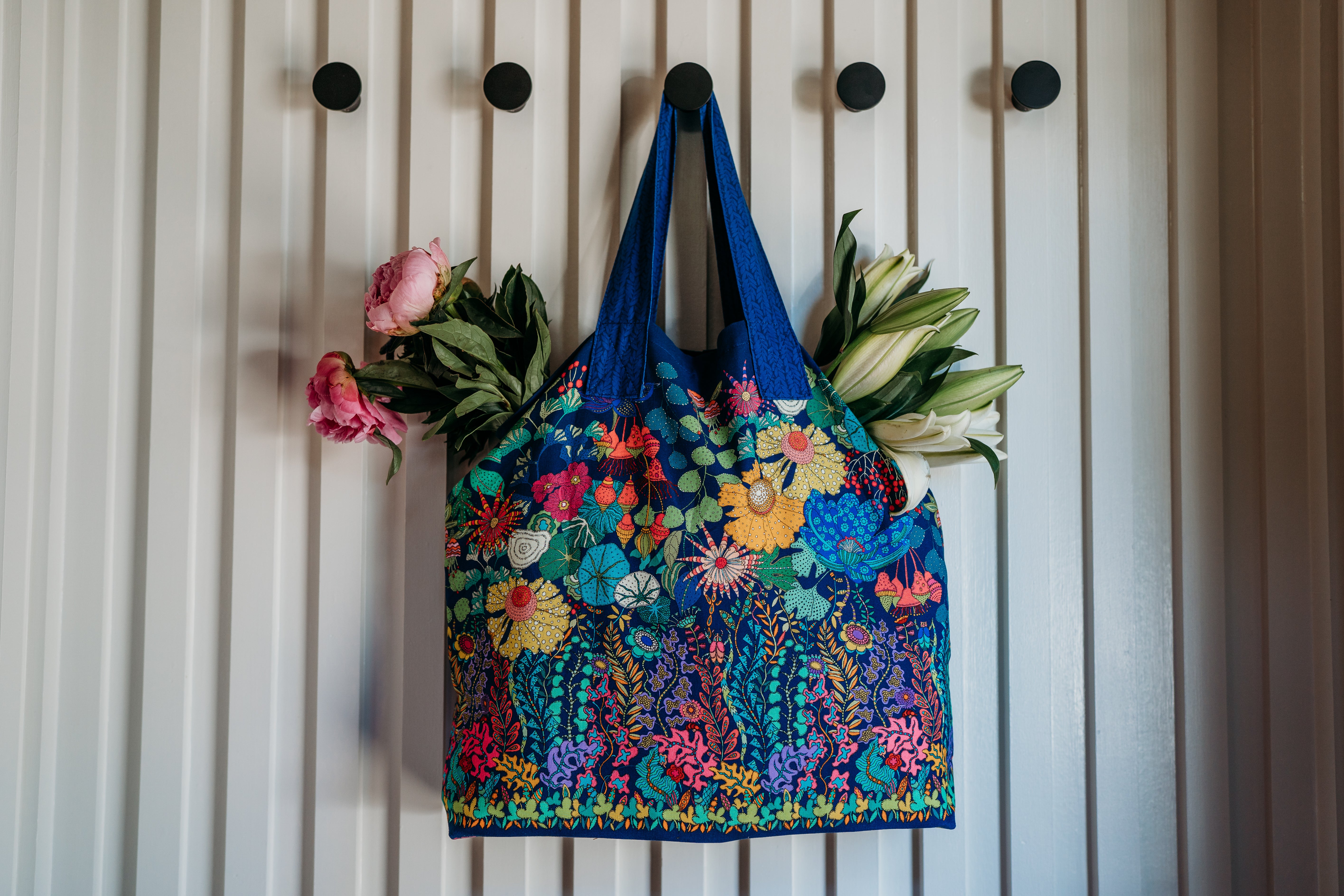 Colorful floral-patterned bag hanging on a white wall with flowers attached.