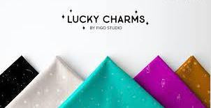At the top of the image and centered is the text "Lucky Charms by Figo Studio." Along the bottom are five fabric cuts folded into triangles, point up like mountains. The fabrics are black, gray, aqua, magenta, and burnt orange.