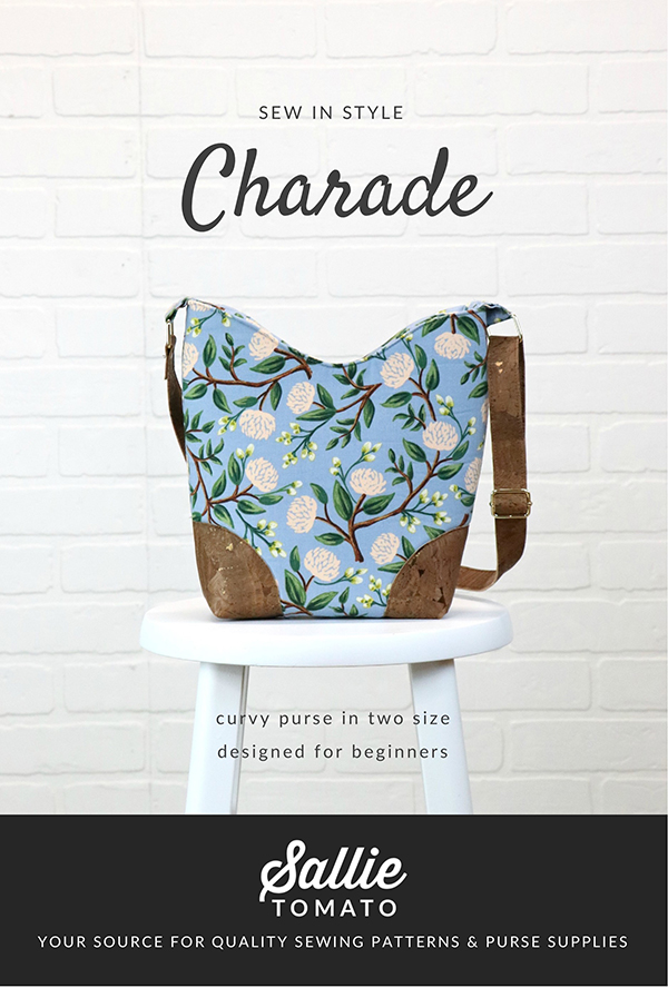 Front and center is a blue purse with a white and green floral print accented with a brown leather strap and brown leather bottom. It sits in a white stool in front of a white brick wall. Above the purse is the text “sew in style; Charade.”