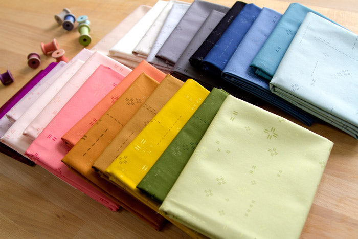 The image shows over a dozen fabric cuts overlapping each other on a table with bobbins to the side.