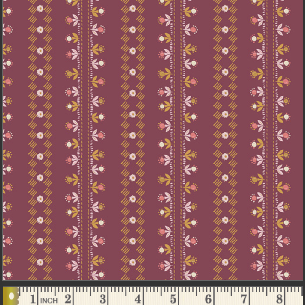 A close-up of a fabric pattern featuring vertical stripes with small floral and geometric motifs in pink, white, mustard yellow, and olive green on a dusty burgundy background. A measuring ruler is visible along the bottom edge to indicate scale.