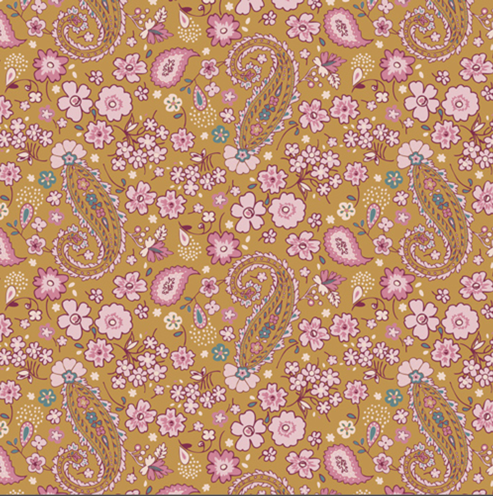 A close-up of a floral and paisley patterned fabric or wallpaper sample on a mustard yellow background, with pink flowers, pink and blue paisley motifs, and a white inch ruler along the bottom edge for scale.