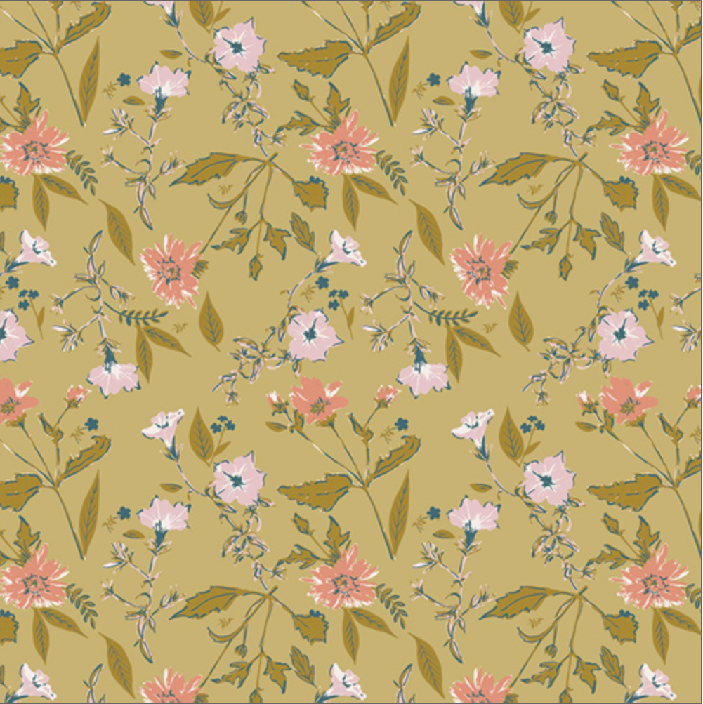 A close-up of a floral fabric pattern on a mustard yellow background, featuring pink flowers, light pink blossoms, and olive green leaves. A black ruler with white markings is visible along the bottom edge to show scale.