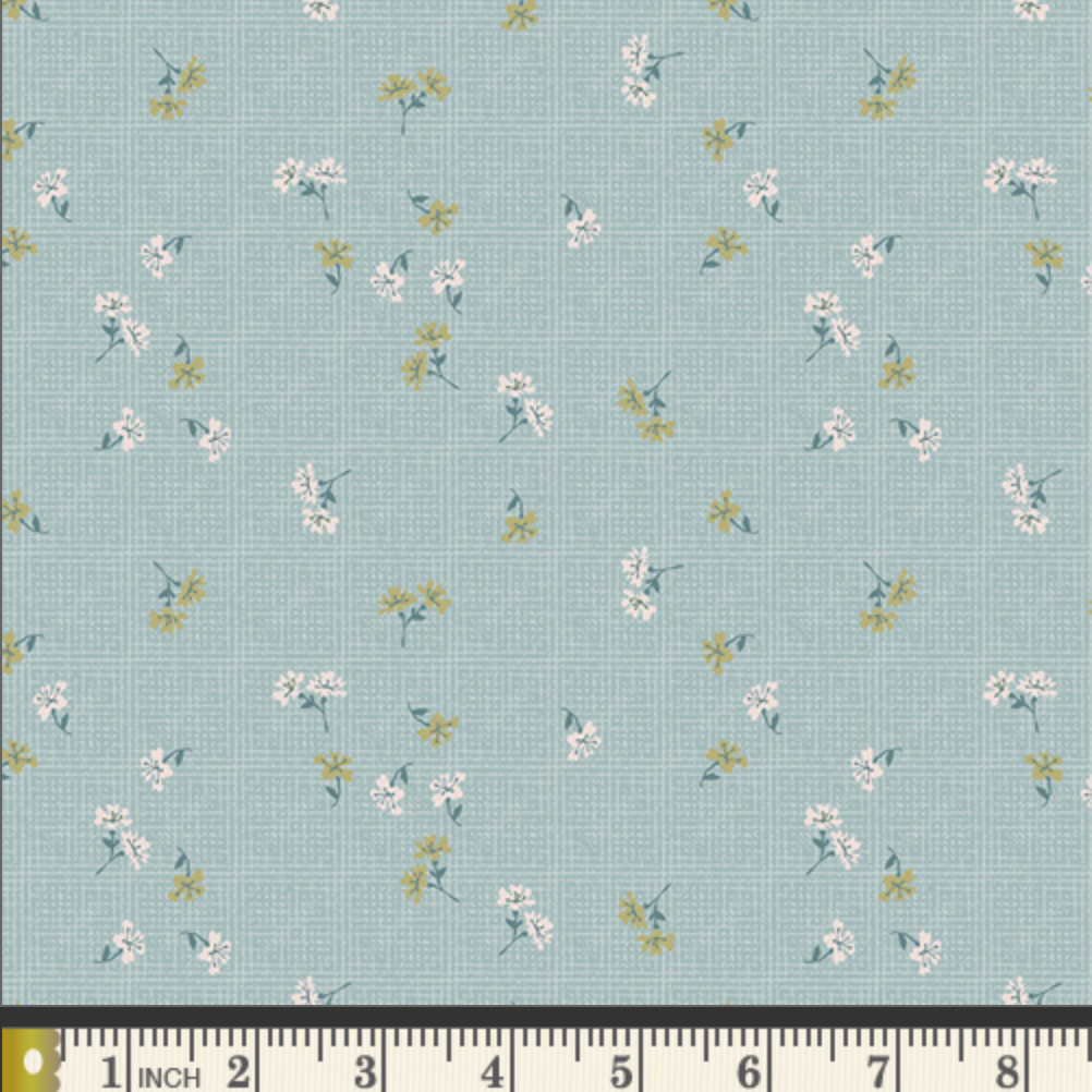 A fabric pattern swatch showing a light blue-green background with a small-scale floral print in white, yellow, and green, with a measuring ruler along the bottom edge.