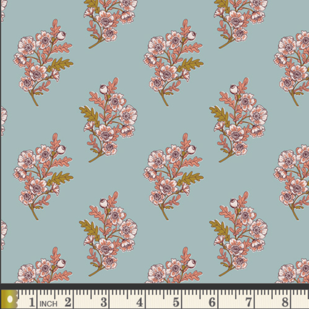 A repeating floral pattern on a dusty blue background, featuring pink blossoms with green and brown leaves and stems. A measuring ruler is visible along the bottom edge to show scale.
