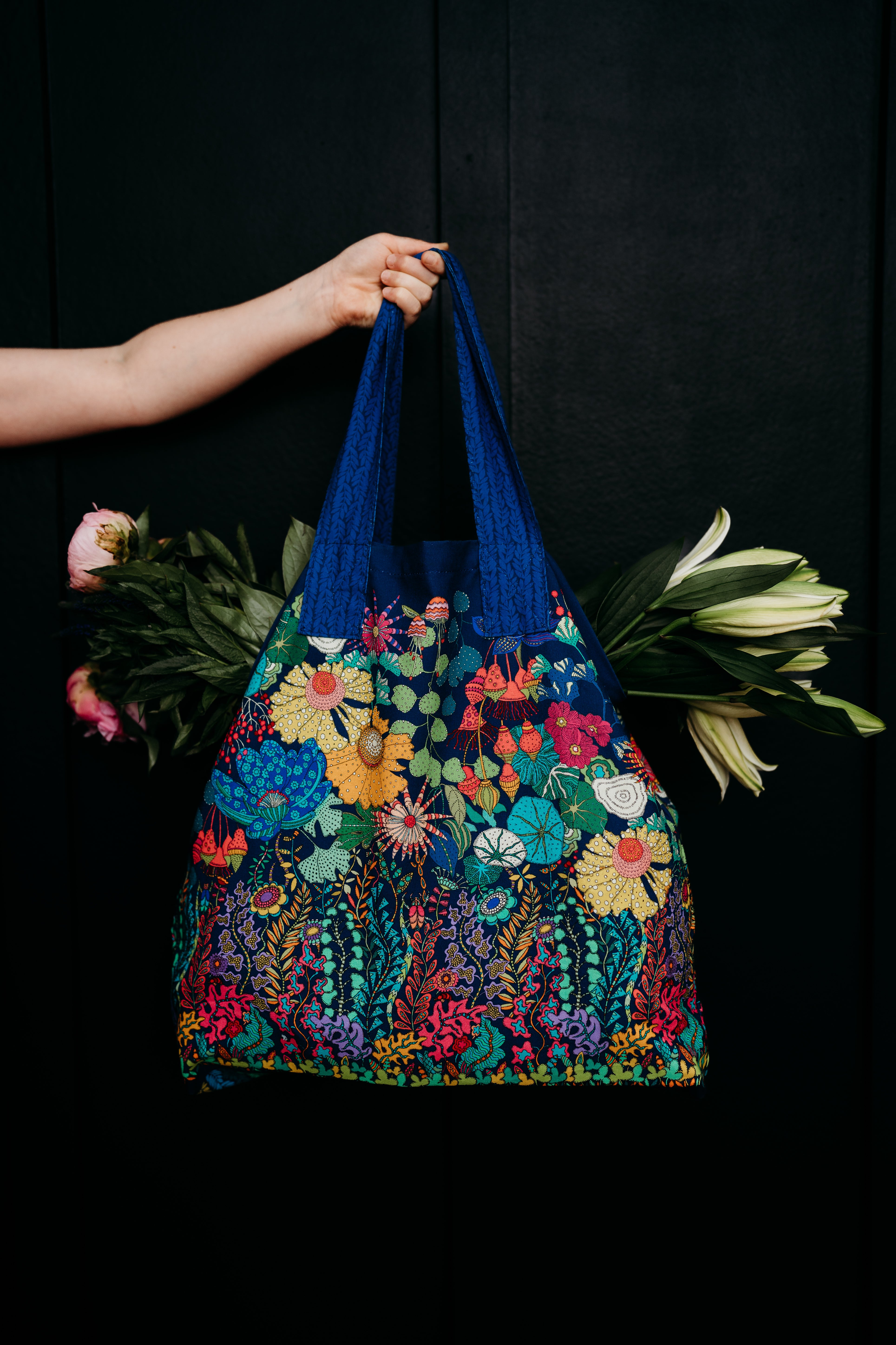 Colorful floral-patterned bag held by a hand against a black background