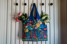 Colorful floral-patterned bag hanging on a white wall with flowers attached.