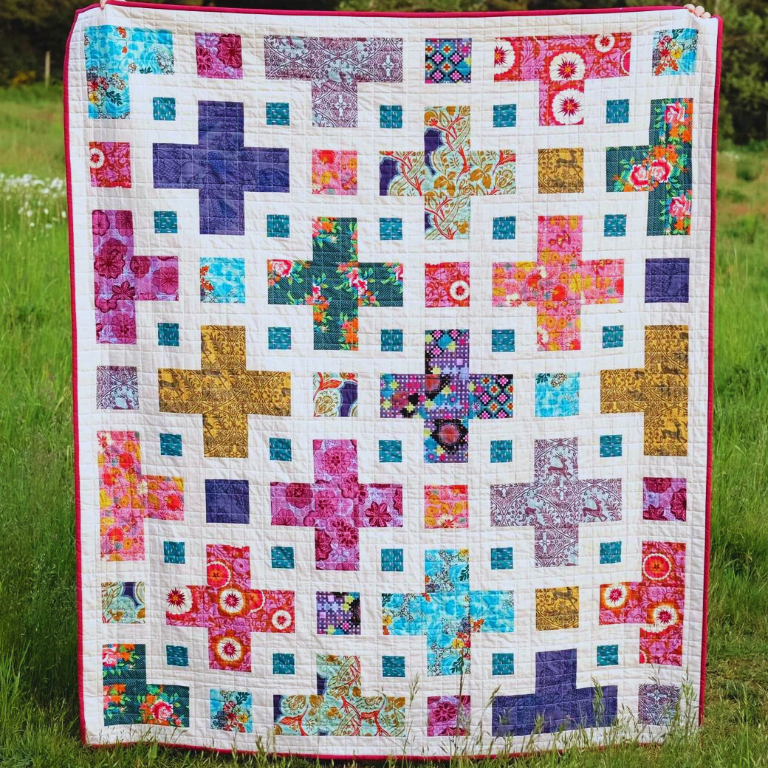 A quilt with a multicolored patchwork design, featuring a variety of geometric shaped patches and a pink border.